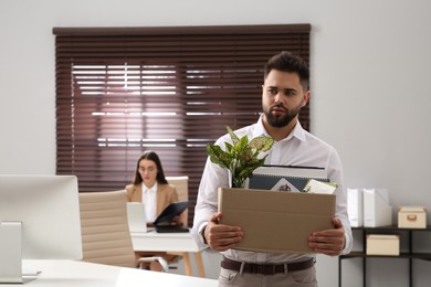 Upset dismissed man carrying box with personal stuff in office