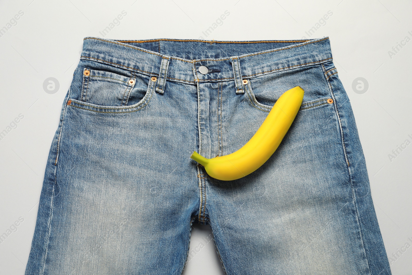 Photo of Men jeans with banana on light grey background, top view. Potency concept