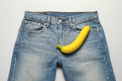 Photo of Men jeans with banana on light grey background, top view. Potency concept