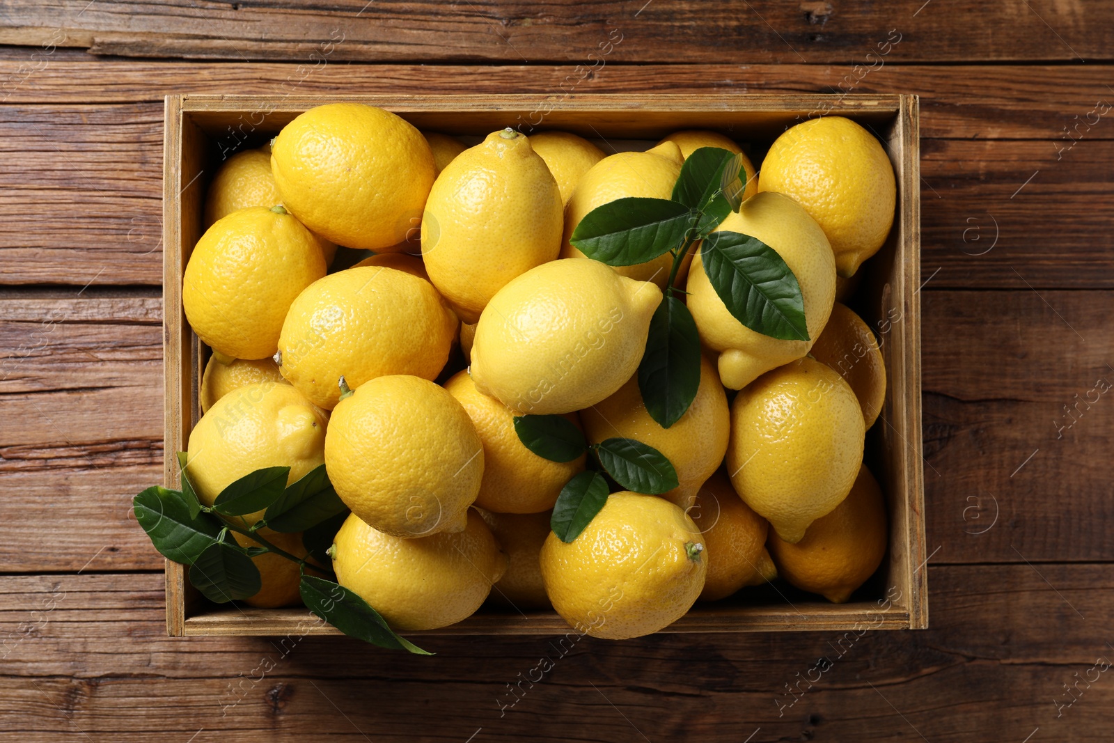 Photo of Fresh lemons in crate on wooden table, top view