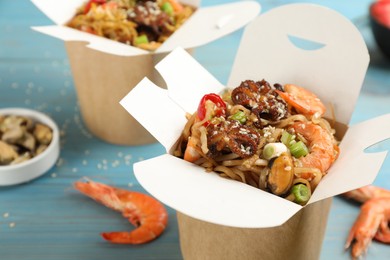 Photo of Boxes of wok noodles with seafood on light blue wooden table, closeup