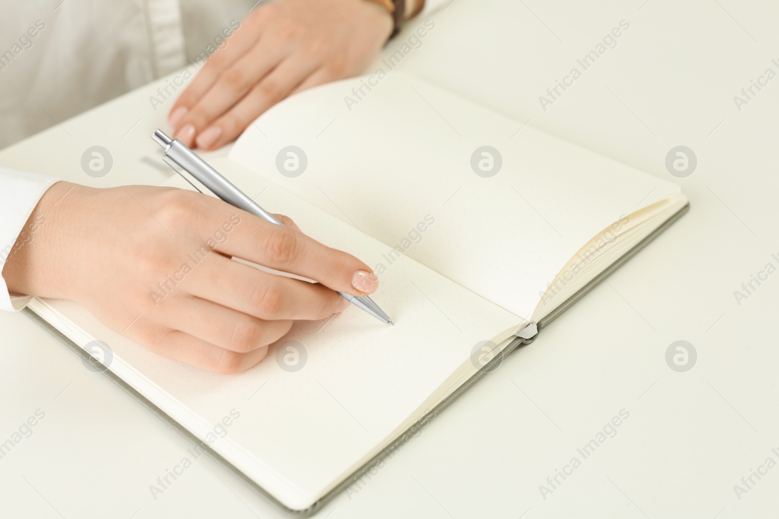 Photo of Woman writing in notebook at white table, closeup