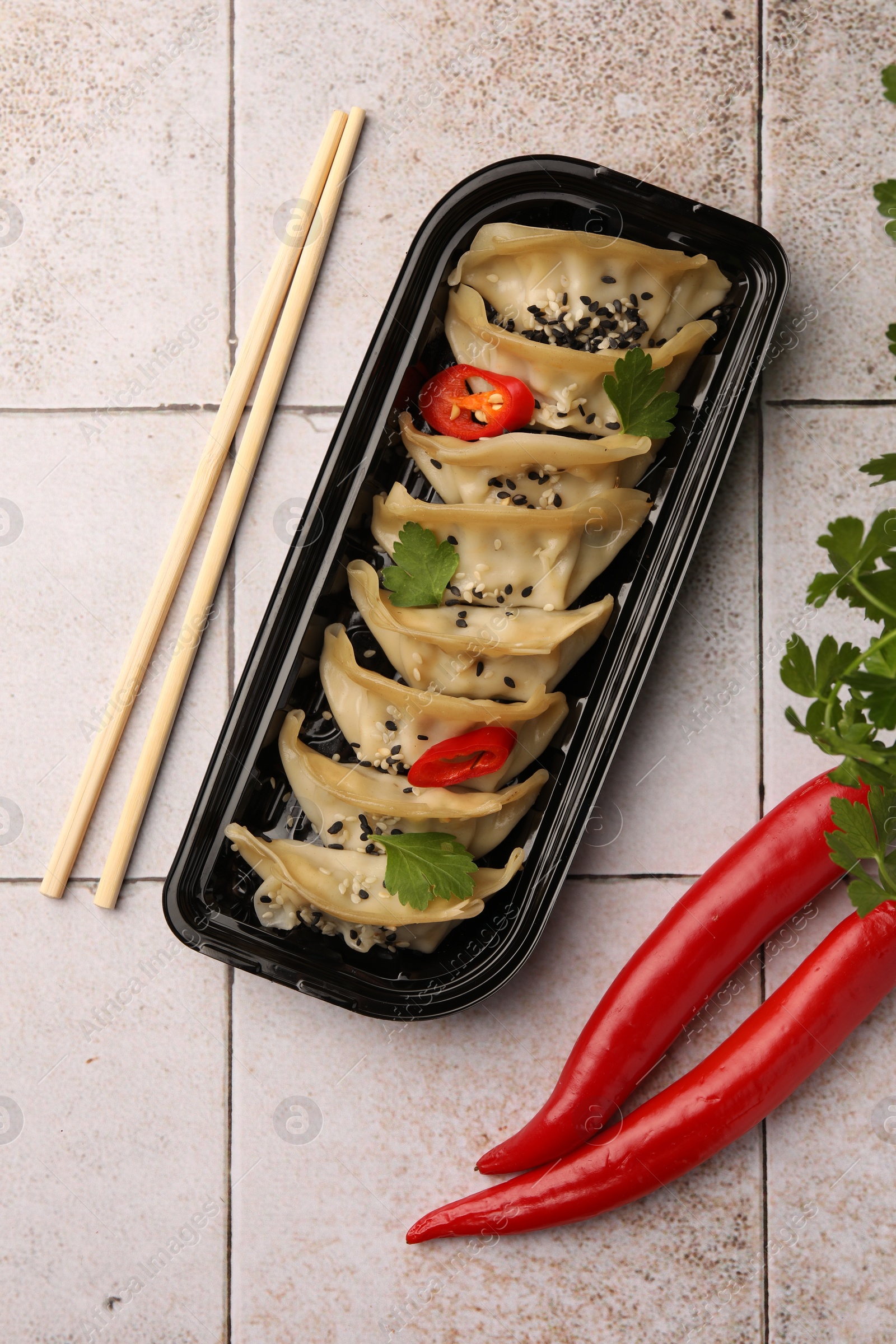 Photo of Delicious gyoza (asian dumplings) with chili peppers, parsley and chopsticks on light tiled table, flat lay