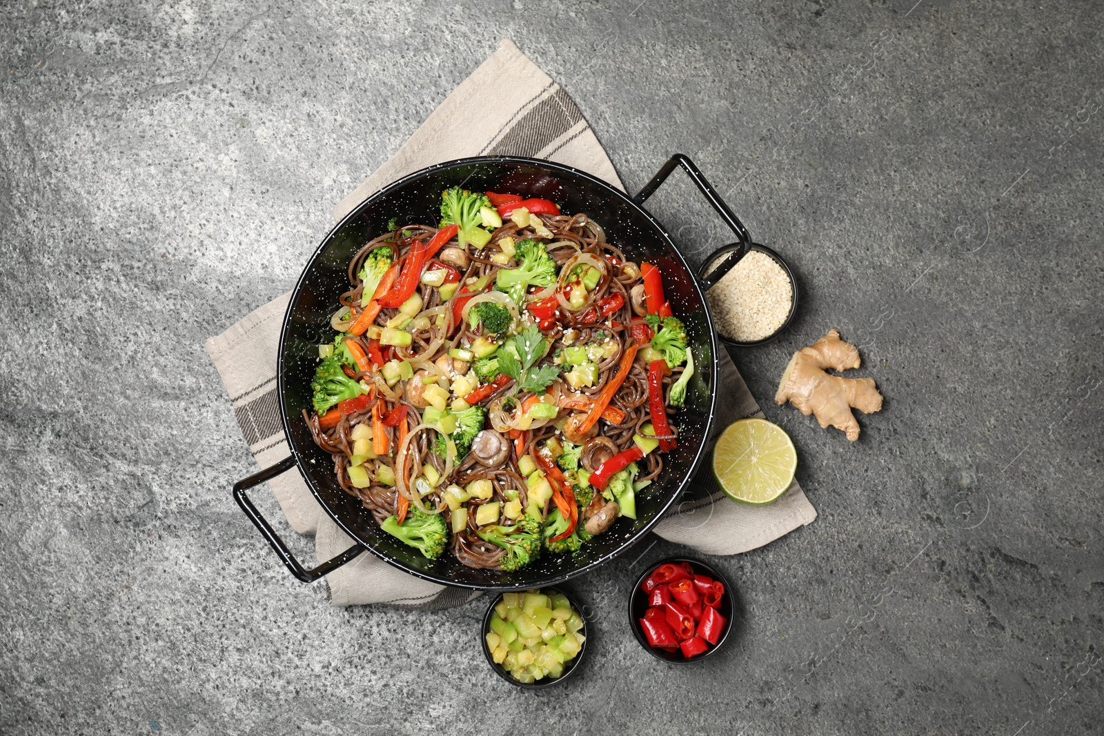 Photo of Wok with noodles, mushrooms, vegetables and other products on grey table, flat lay