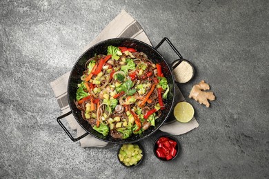 Photo of Wok with noodles, mushrooms, vegetables and other products on grey table, flat lay