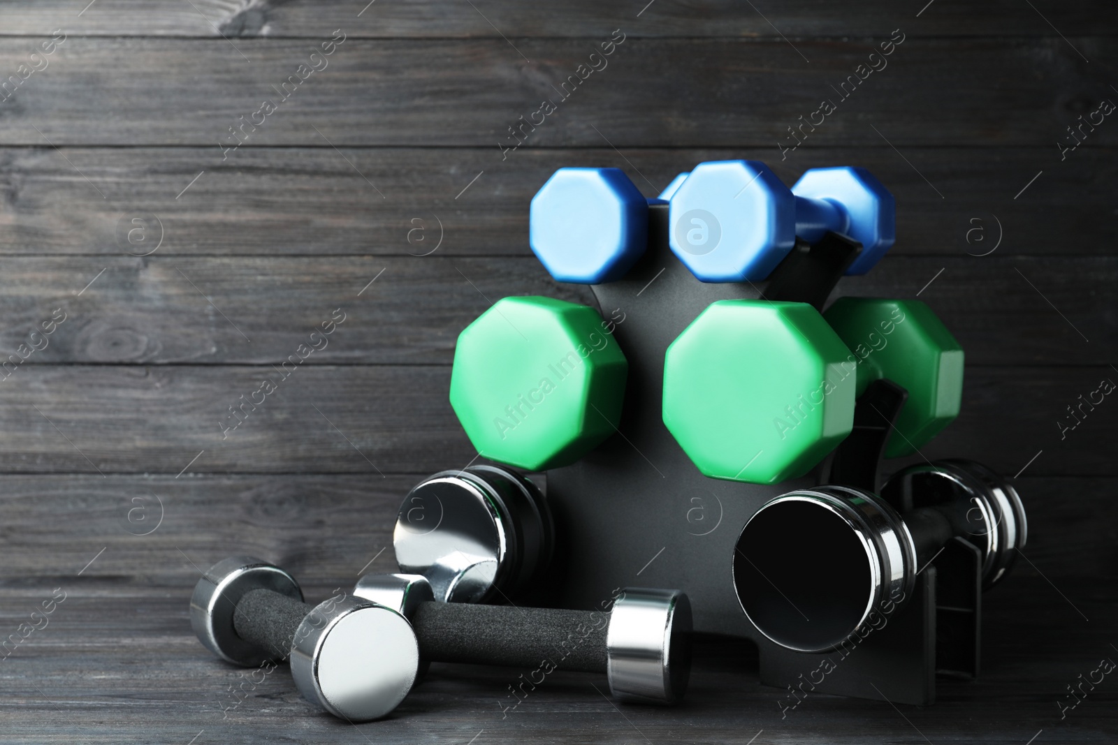 Photo of Rack with different dumbbells on black wooden background. Space for text