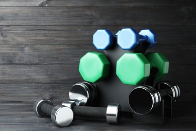 Photo of Rack with different dumbbells on black wooden background. Space for text