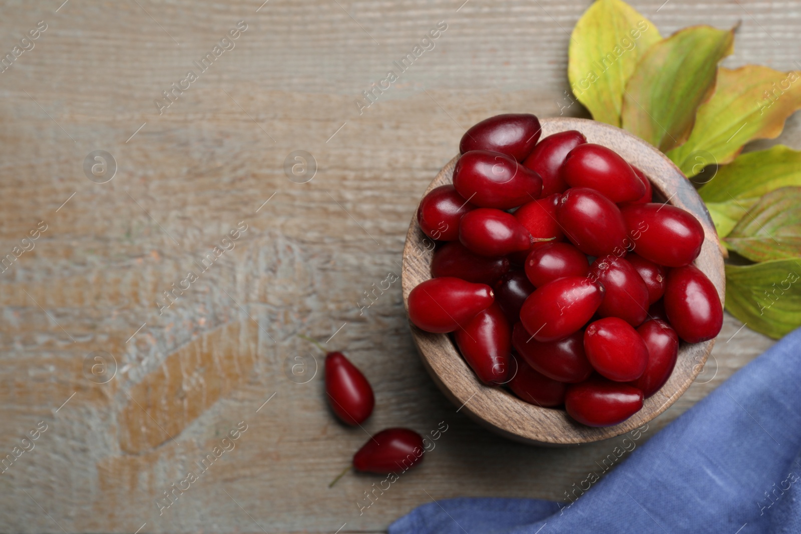 Photo of Fresh ripe dogwood berries with green leaves on wooden table, flat lay. Space for text