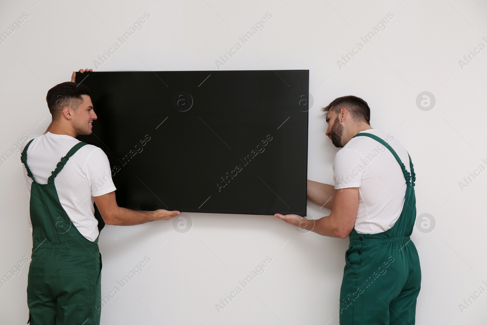 Photo of Professional technicians installing modern flat screen TV on wall indoors