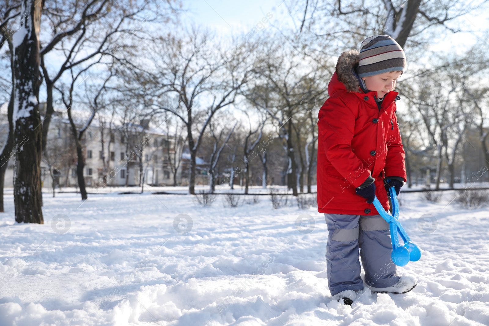 Photo of Cute little boy playing with snowball maker in park on sunny winter day. Space for text