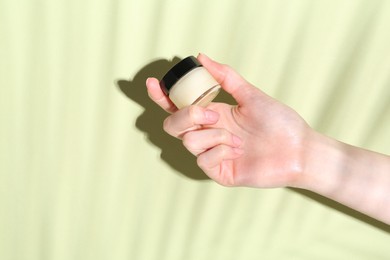 Woman holding jar of cream on green background, closeup. Space for text