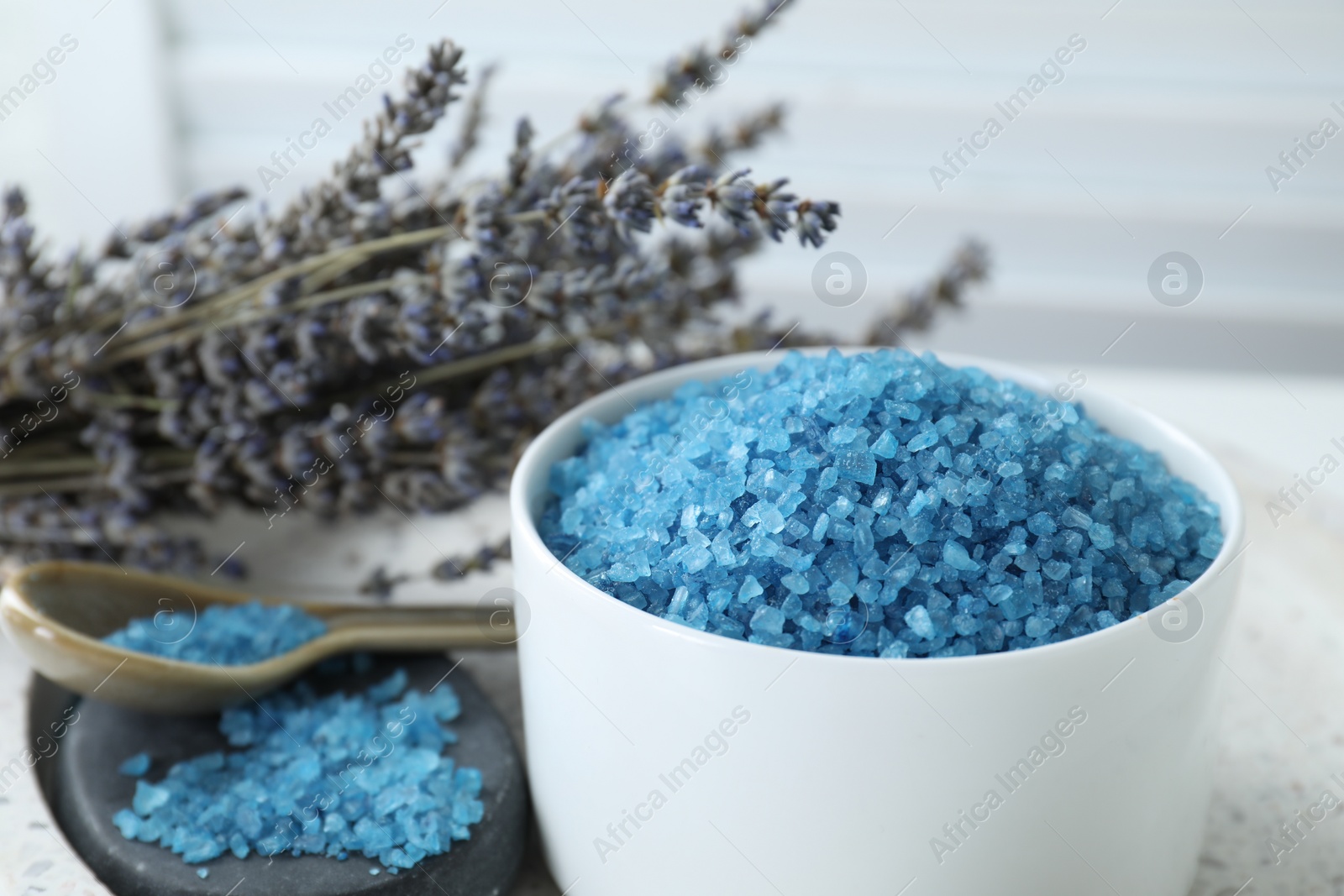 Photo of Bowl with blue sea salt and lavender flowers on table, closeup