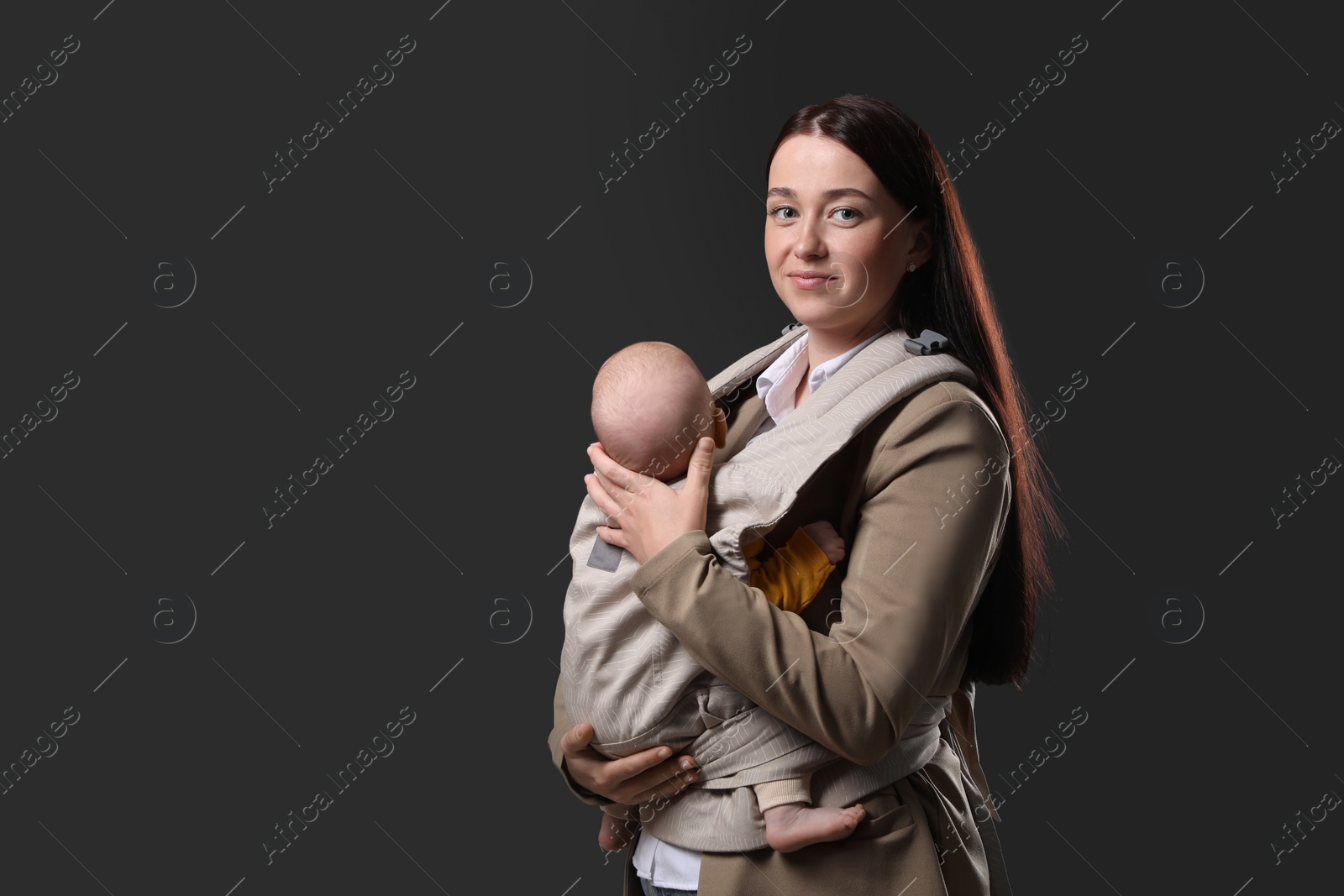 Photo of Mother holding her child in baby carrier on black background. Space for text