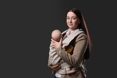 Photo of Mother holding her child in baby carrier on black background. Space for text