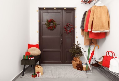 Photo of Christmas wreaths hanging on wooden door, festive decoration and outwear indoors