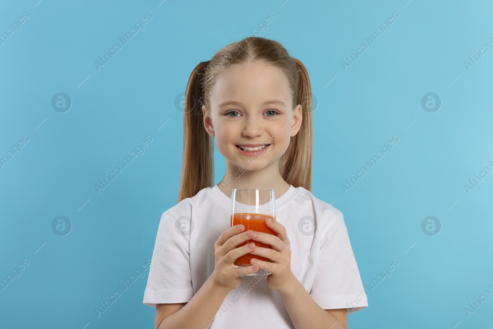 Photo of Cute little girl with glass of fresh juice on light blue background