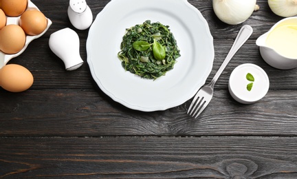 Photo of Flat lay composition with cooked spinach on black wooden table. Healthy food