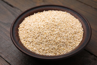 Photo of Raw barley groats in bowl on wooden table, closeup