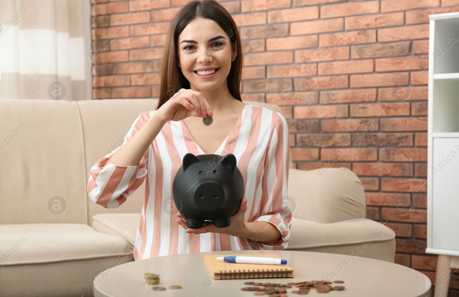 Photo of Happy young woman with piggy bank and money at home