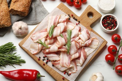 Slices of raw bacon and fresh products on white marble table, flat lay