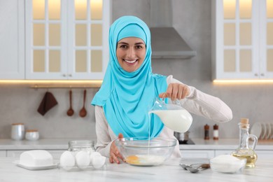 Muslim woman making dough at white table in kitchen