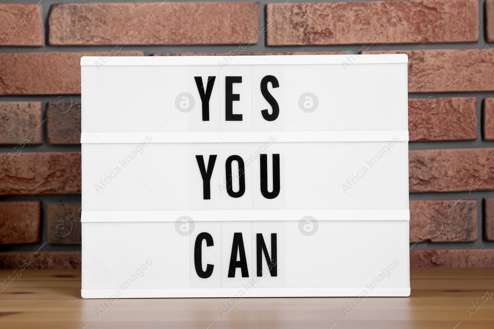 Photo of Lightbox with phrase Yes You Can on table against brick wall. Motivational quote