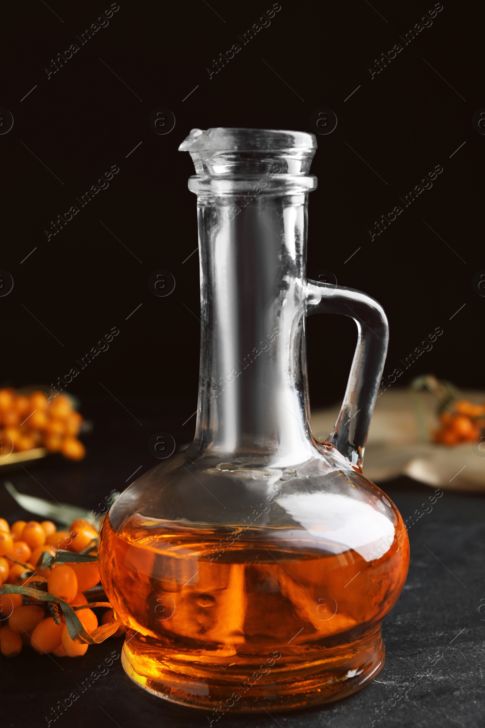 Photo of Ripe sea buckthorn and jug of essential oil on black table