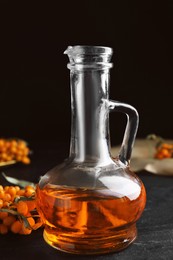 Ripe sea buckthorn and jug of essential oil on black table