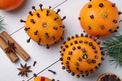 Photo of Pomander balls made of tangerines with cloves and fir branches on white wooden table, flat lay