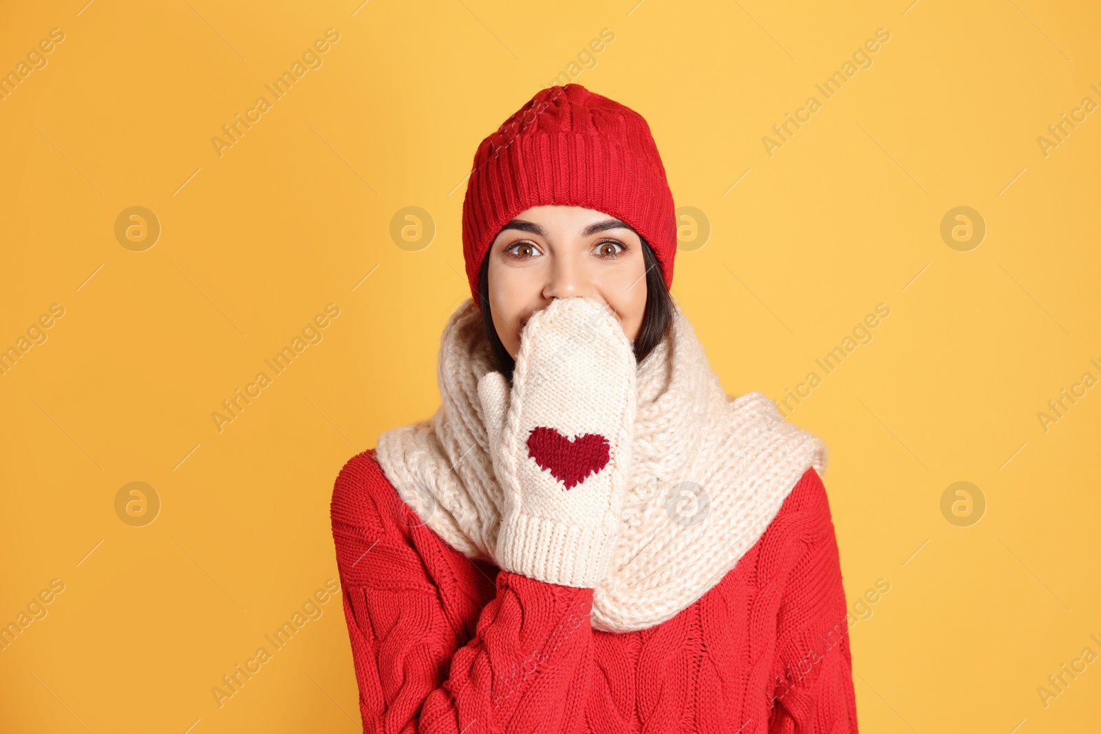 Photo of Young woman wearing warm sweater, scarf, mittens and hat on yellow background. Winter season