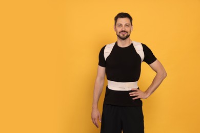 Photo of Handsome man with orthopedic corset on orange background, space for text