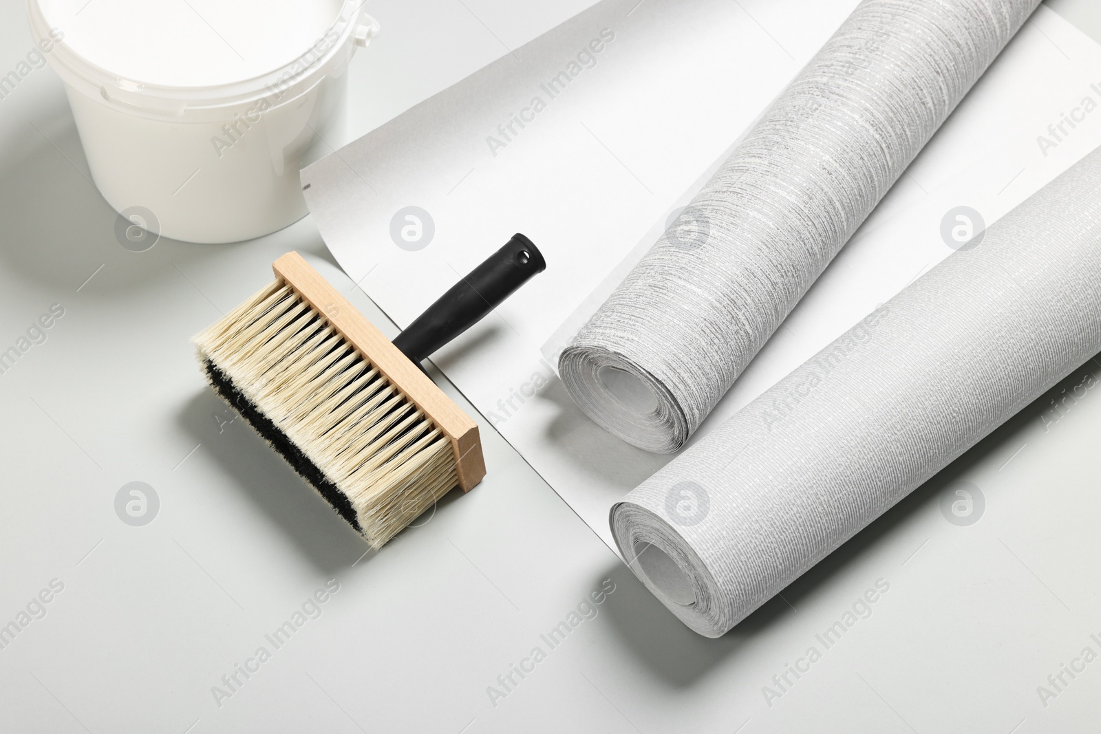 Photo of Different wallpaper rolls, brush and bucket with glue on light grey background