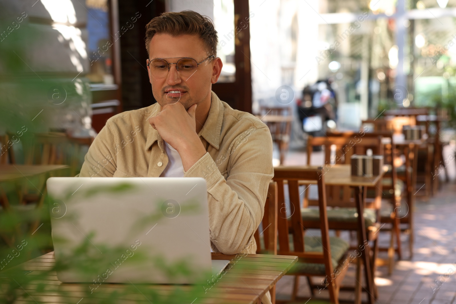 Photo of Handsome man working on laptop at table in outdoor cafe. Space for text