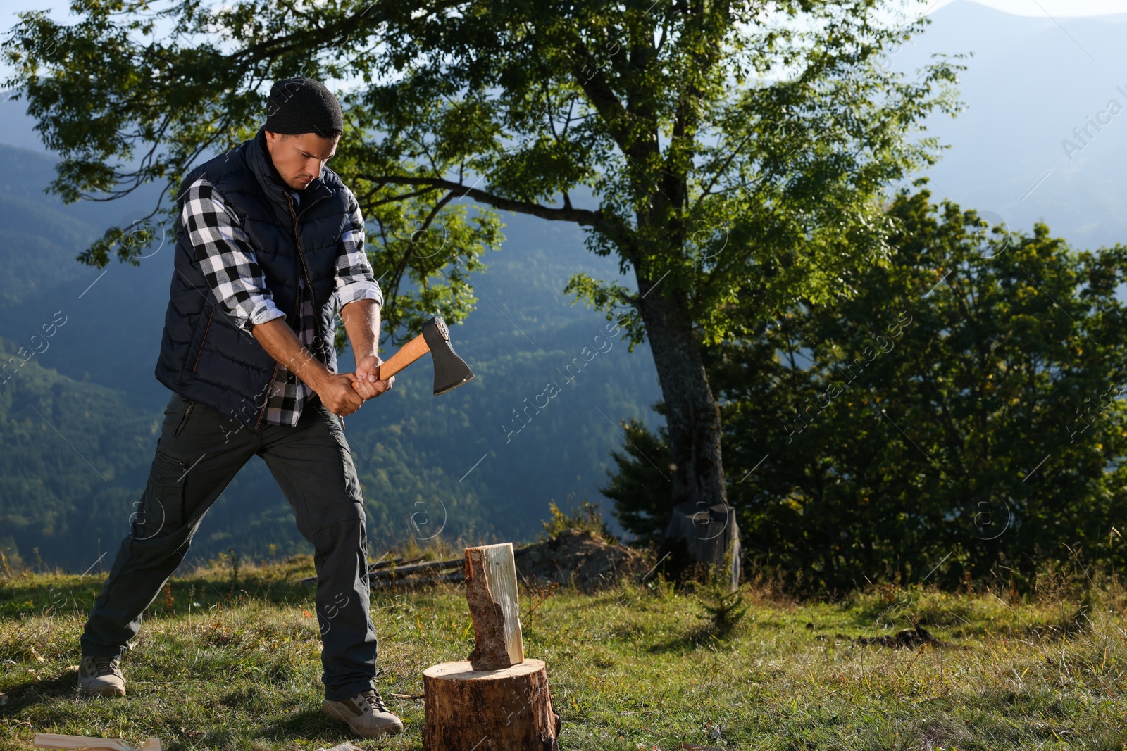 Photo of Handsome man with axe cutting firewood in mountains