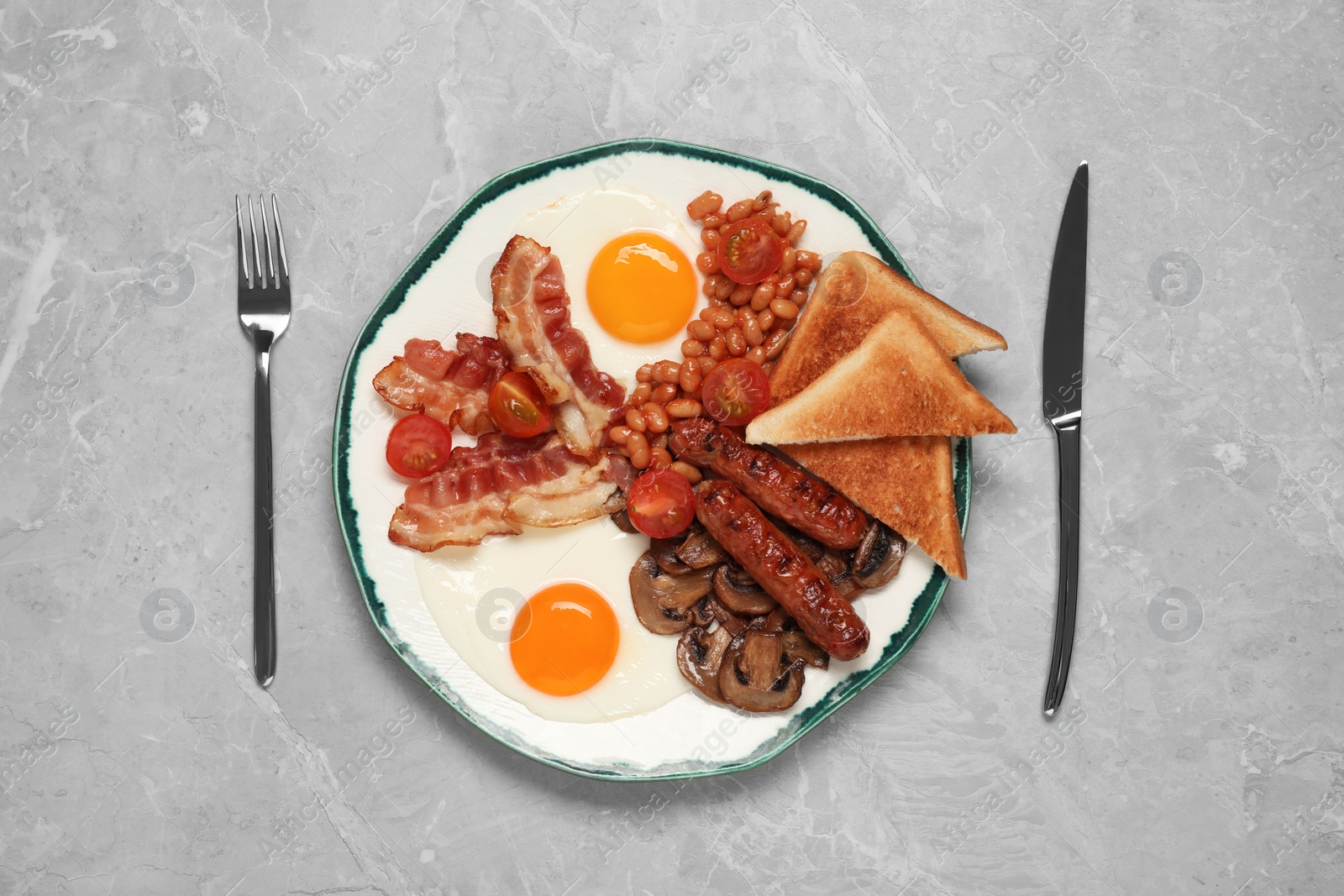 Photo of Plate of fried eggs, mushrooms, beans, bacon, sausages and toasts served on grey marble table, flat lay. Traditional English breakfast