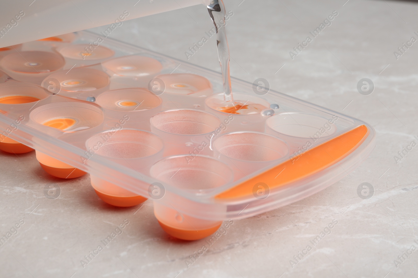 Photo of Pouring water into ice cube tray on table, closeup