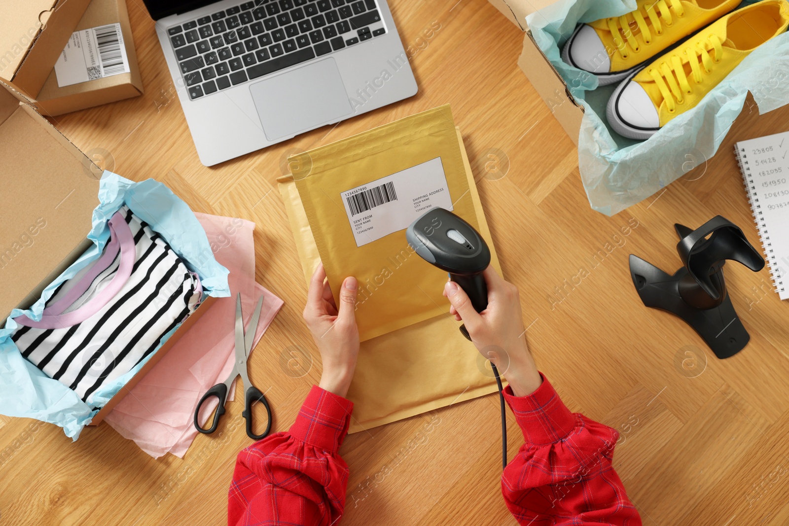 Photo of Woman with scanner reading parcel barcode at wooden table, top view. Online store