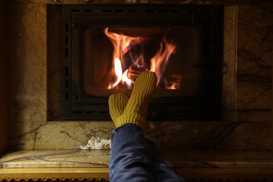Photo of Woman in warm socks resting near fireplace indoors, closeup