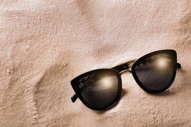 Stylish sunglasses on white sand, top view. Space for text