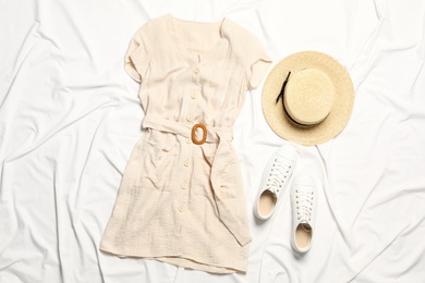 Stylish beige dress, shoes and hat on white fabric, flat lay