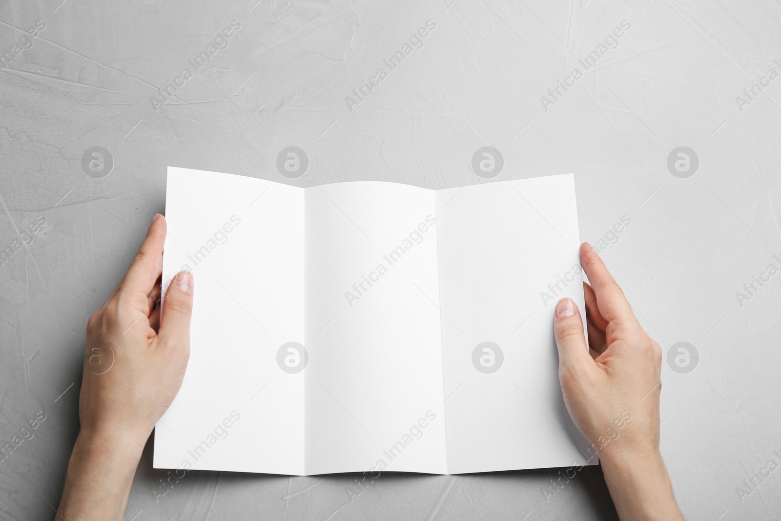 Photo of Young woman holding blank brochure at grey table, top view. Mock up for design