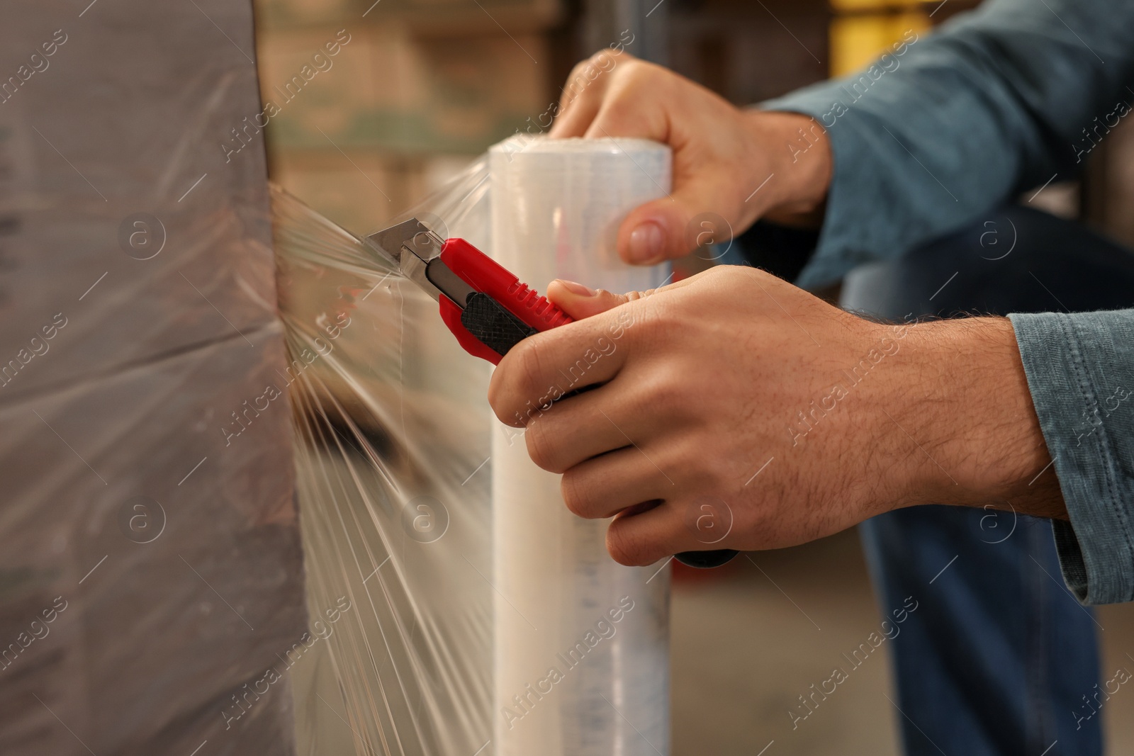 Photo of Worker wrapping boxes in stretch film at warehouse, closeup