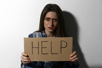 Photo of Abused young woman with sign HELP near white wall. Domestic violence concept