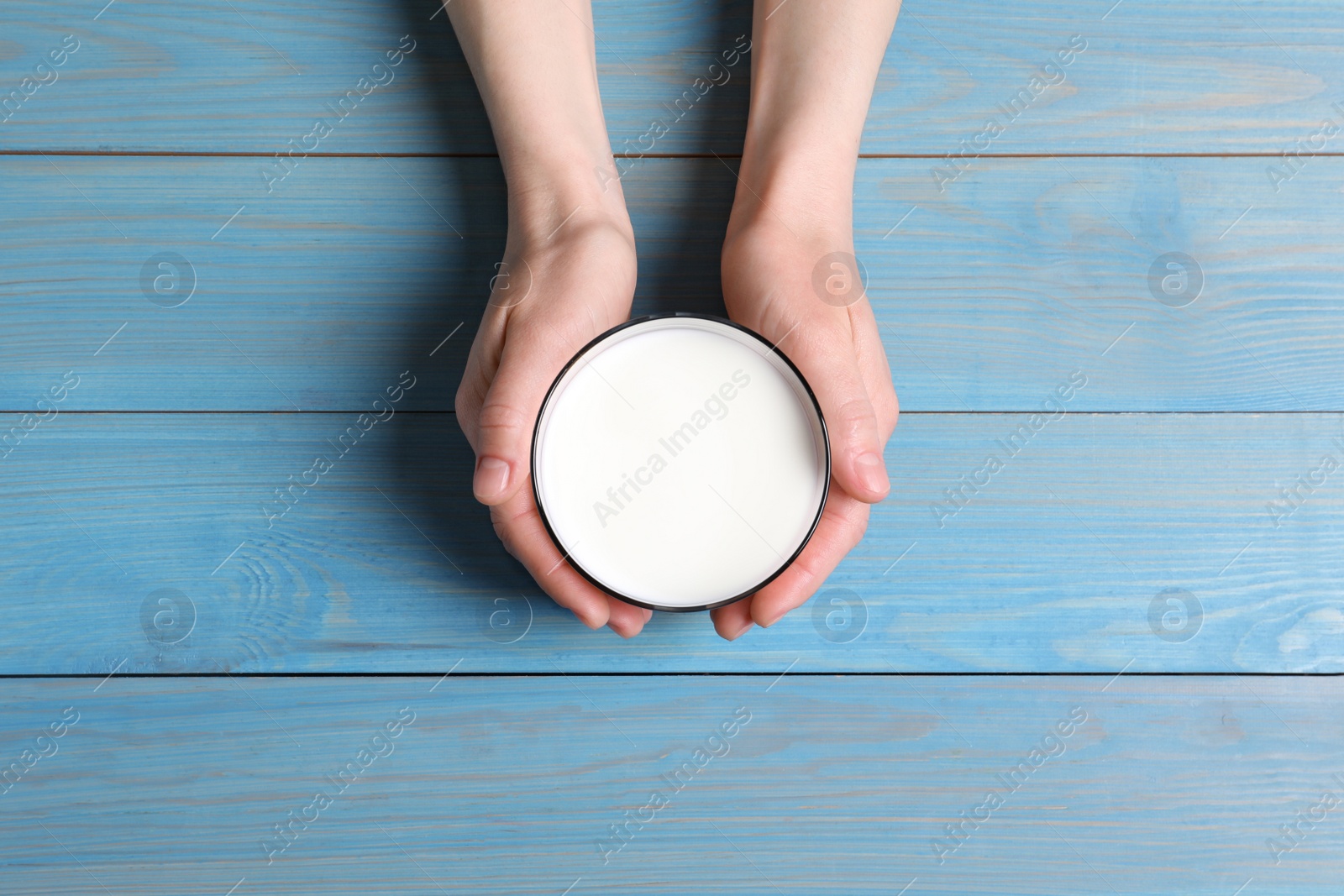 Photo of Woman holding glass of milk at light blue wooden table, top view