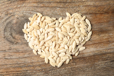 Photo of Heart made of raw cucumber seeds on wooden background, top view. Vegetable planting
