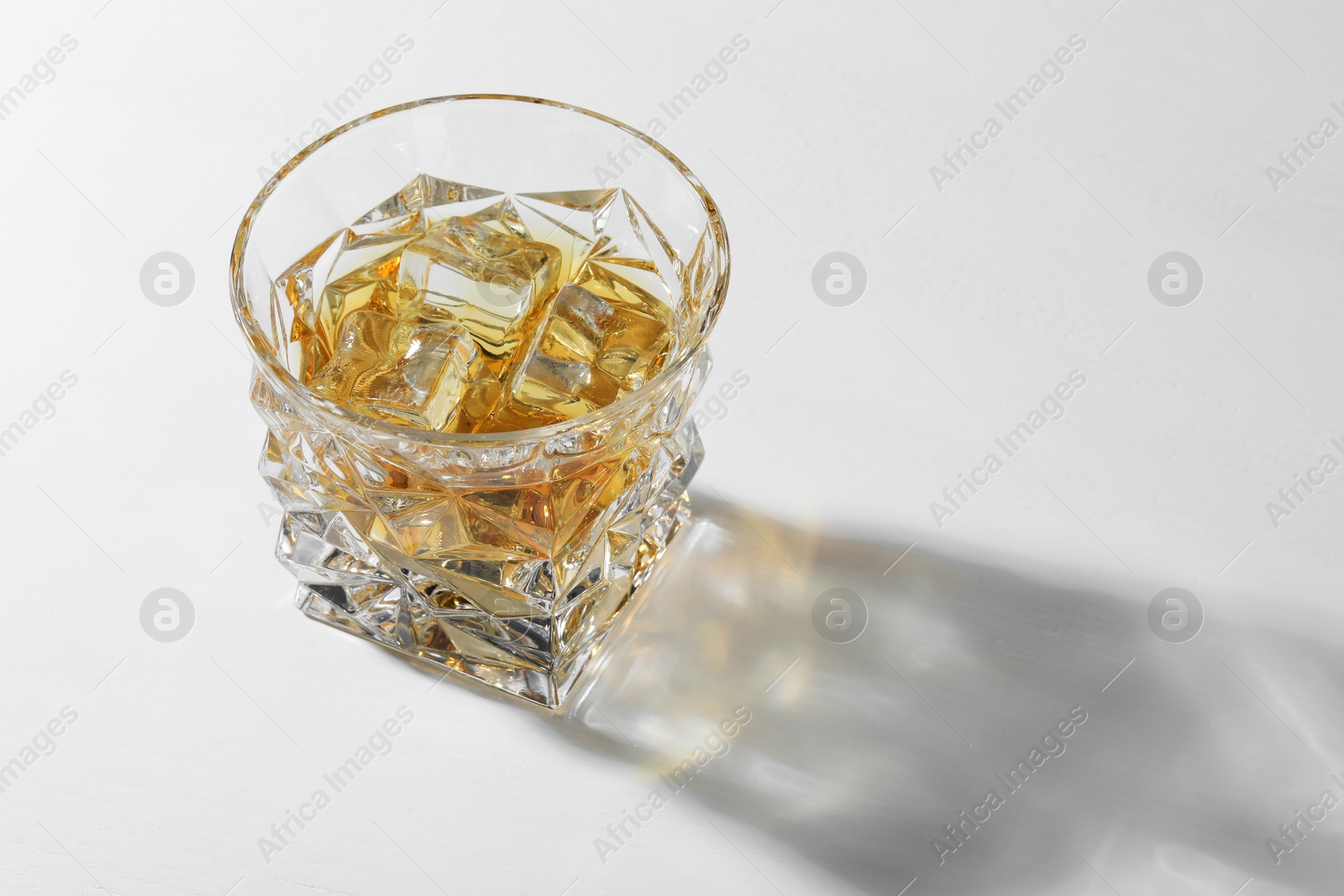 Photo of Whiskey with ice cubes in glass on white table, space for text