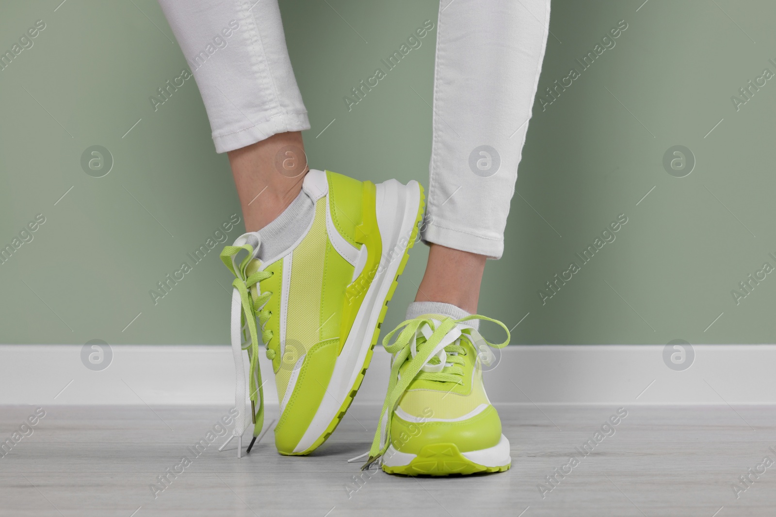 Photo of Woman wearing pair of new stylish sneakers near light green wall, closeup