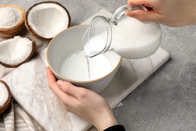 Photo of Woman pouring delicious coconut milk into bowl at light grey table, closeup
