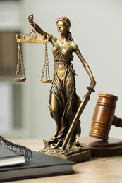 Photo of Figure of Lady Justice, gavel and notebooks on wooden table indoors. Symbol of fair treatment under law