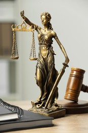 Figure of Lady Justice, gavel and notebooks on wooden table indoors. Symbol of fair treatment under law